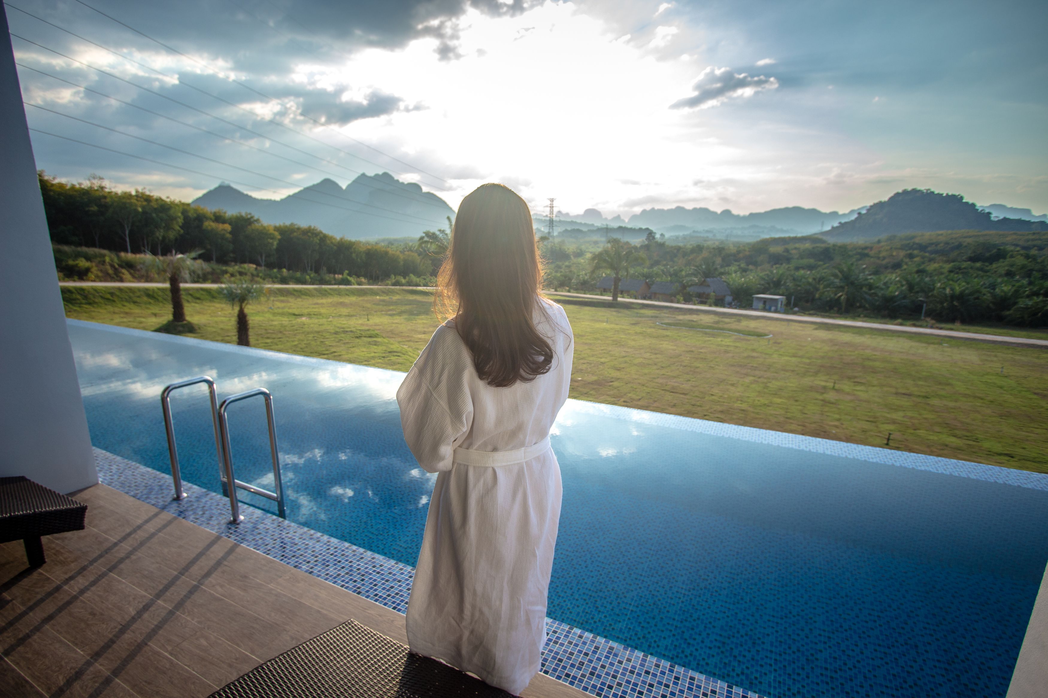 Una persona parada junto a una piscina infinita con vistas a un paisaje cubierto de hierba y montañas a lo lejos.