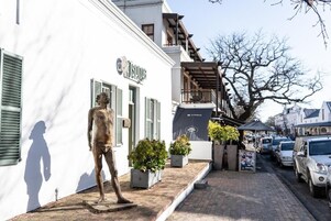 Ruas com um edifício branco, uma estátua e carros estacionados.