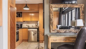 Een compacte keuken met houten kastjes, een inbouwvaatwasser en een spiegel met stenen lijst boven een bureau.
