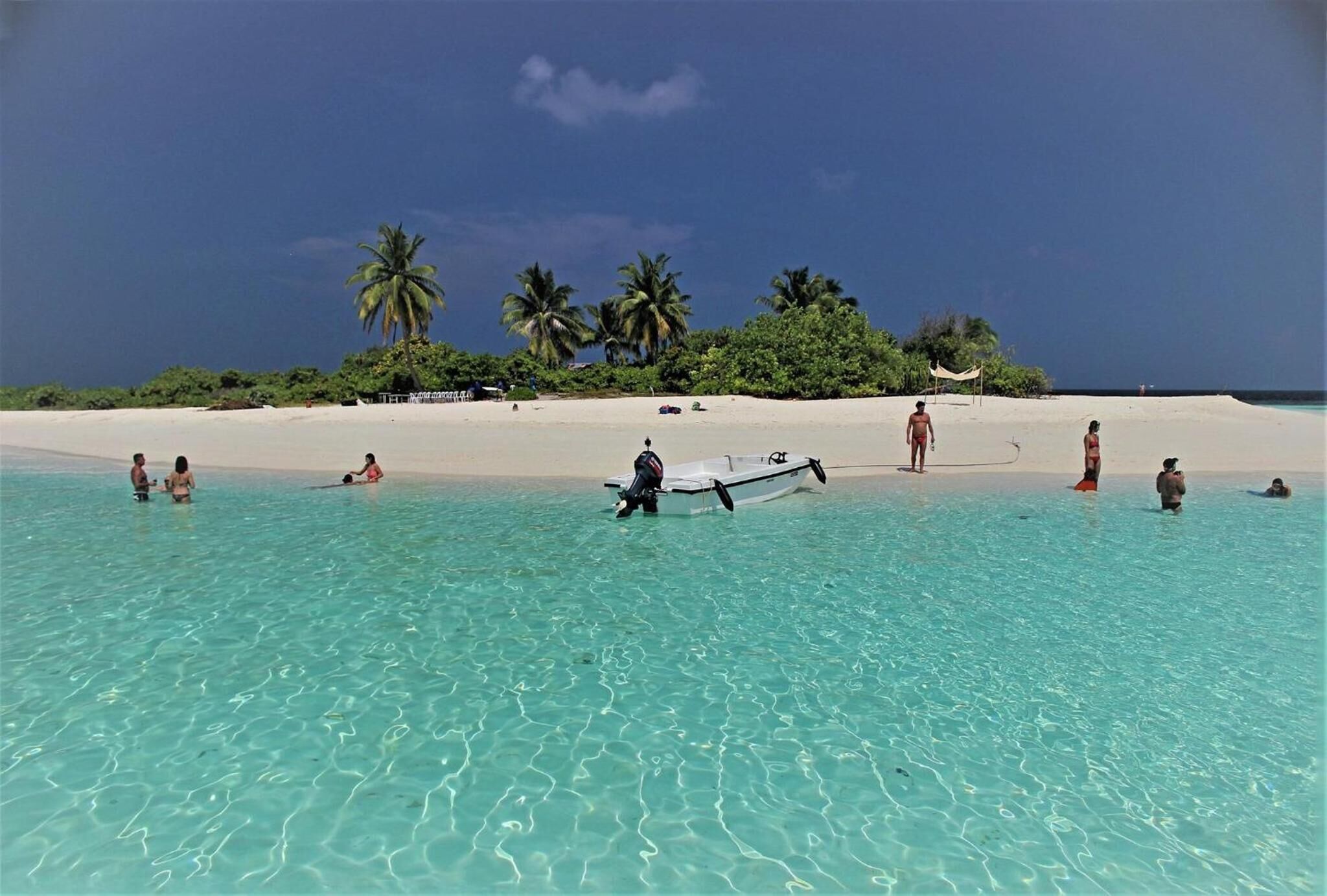 Uma praia com águas turquesa cristalinas, palmeiras e um pequeno barco.
