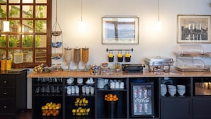 Disposición de bufé con diferentes alimentos, un refrigerador con bebidas y una ventana con plantas.