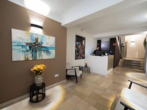 A hotel lobby with a reception desk, a large abstract painting, a vase with flowers, and a staircase leading to another floor. - Smart Stay Hotel Station (Munich)