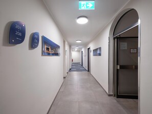 Een hotelgang met genummerde borden, een bord voor de vluchtweg en een deur met een matglasraam.