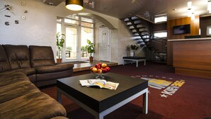 A modern living room with a brown leather sofa, a coffee table with a magazine, and a fruit bowl. There is a staircase, a door leading outside, and a TV mounted on the wall. - Kiev365 (Sofiivska Borschahivka)