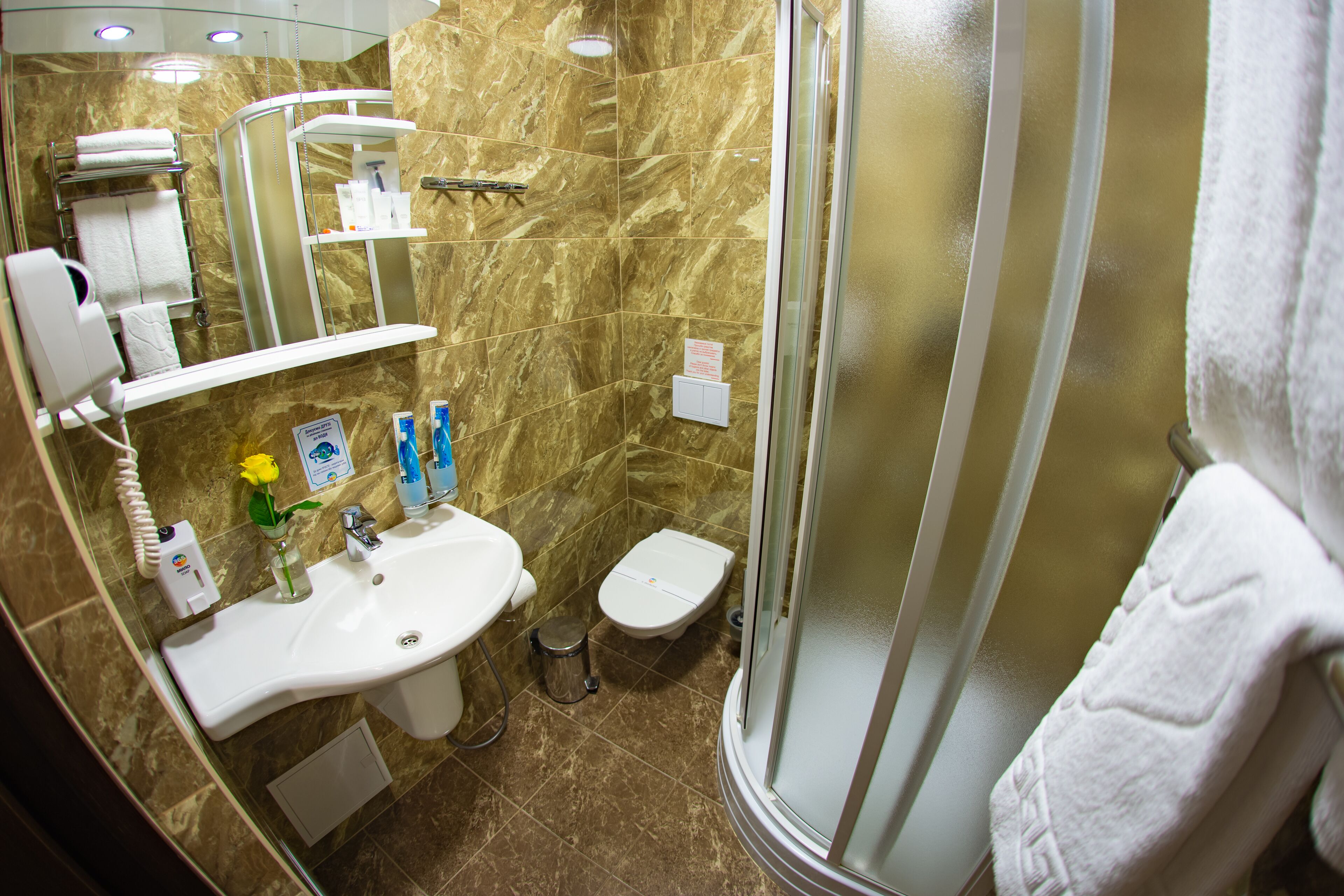A bathroom with a sink, toilet, and shower. There are toiletries on the sink and a towel hanging on the wall.