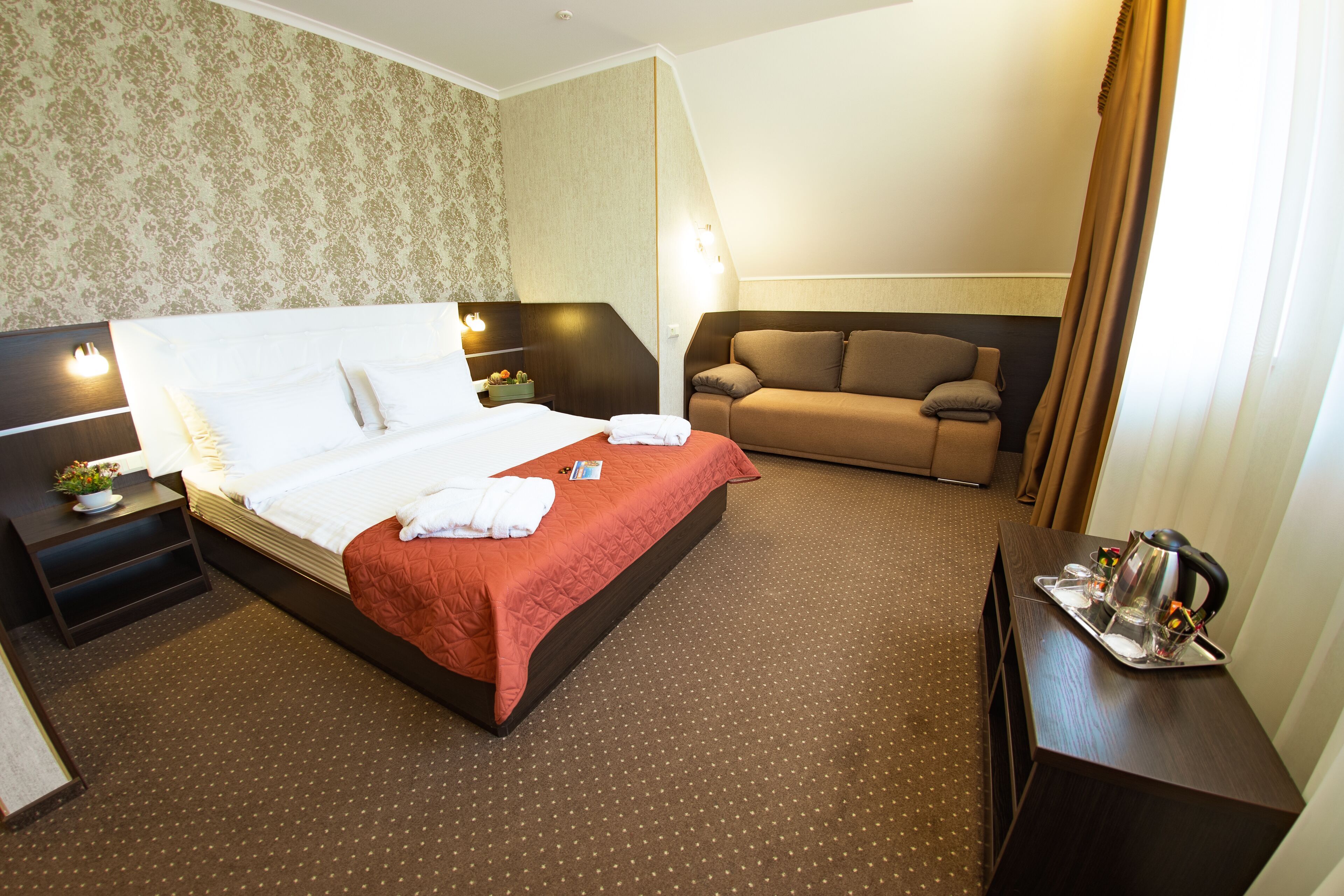 Una habitación de hotel con una cama grande, un sofá, un escritorio con bandeja y una mesita de noche.