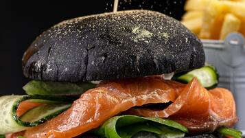 A sandwich with a black bun, salmon, cucumber, and greens, with a side of fries.
