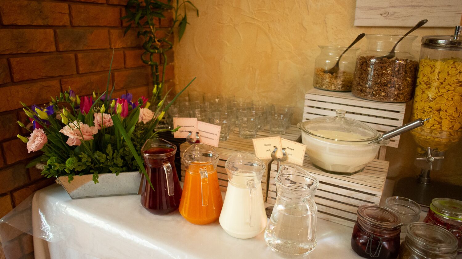 Una barra de desayuno con diversas opciones de comida y bebidas, incluyendo frascos de mermelada, una jarra de jugo de naranja y un tazón de cereal.