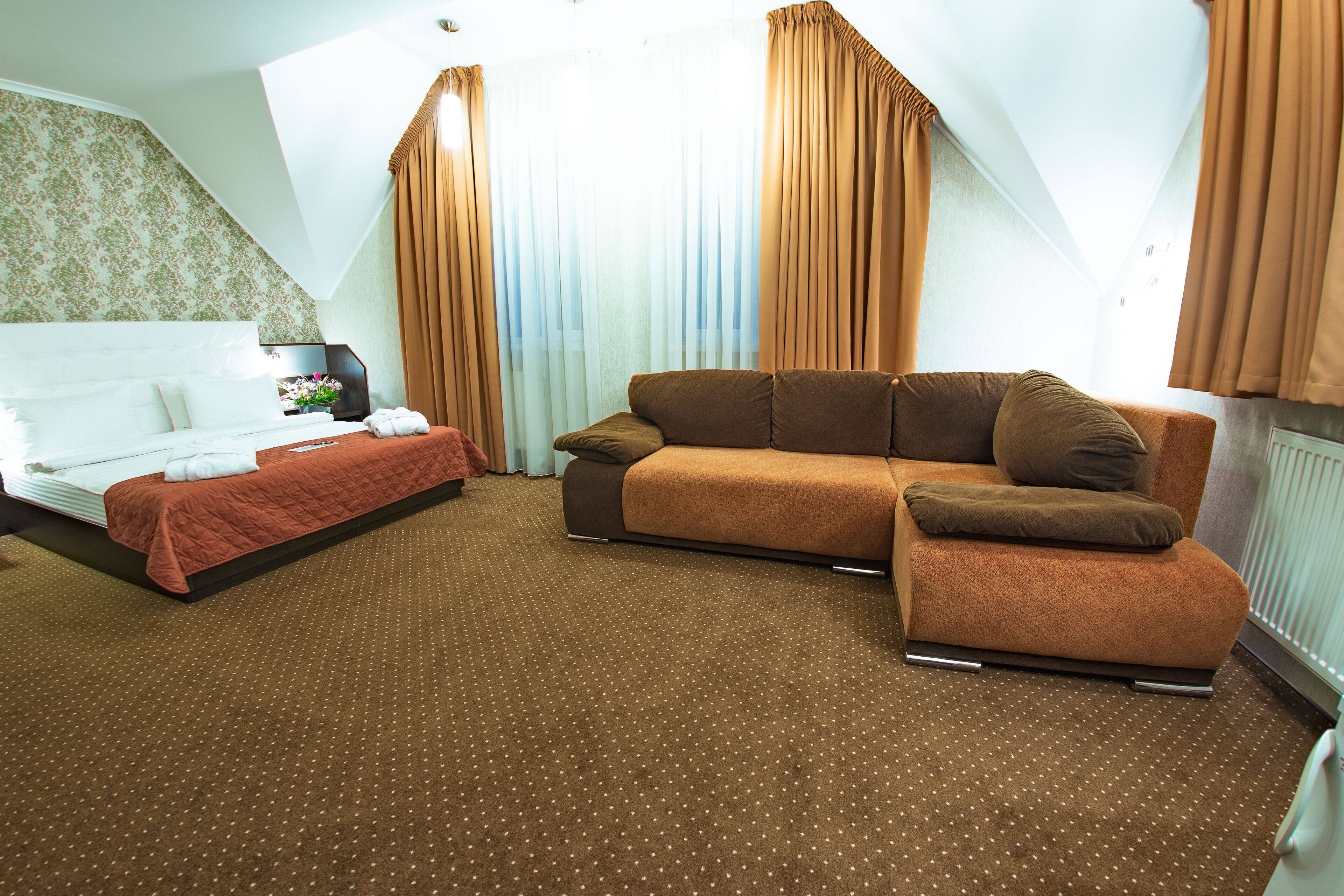 A hotel room with a bed, a sofa, and a large window with curtains.