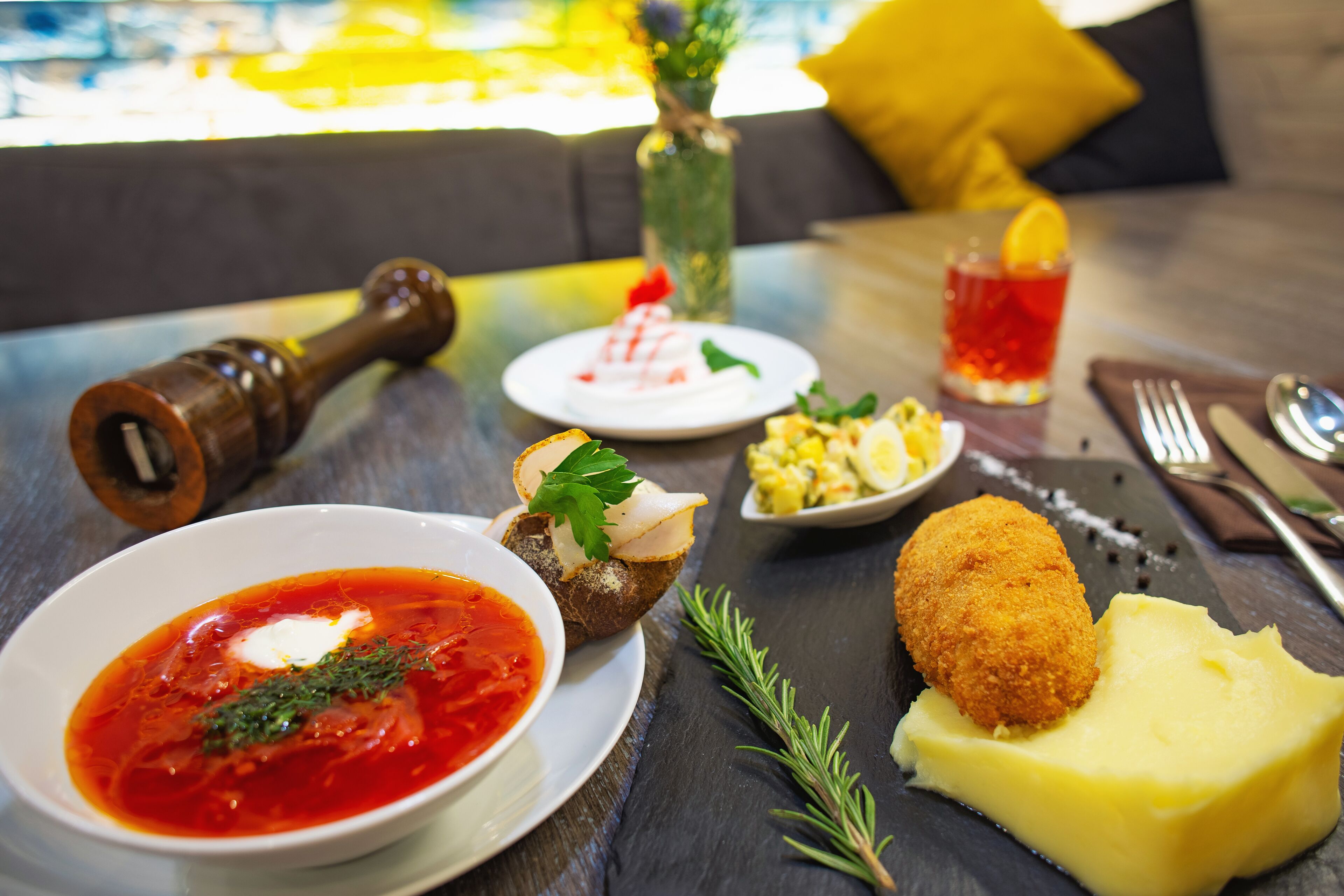 Een eettafel met diverse gerechten, waaronder soep, brood en een kroket, plus een glas rode drank en een zoutvaatje.