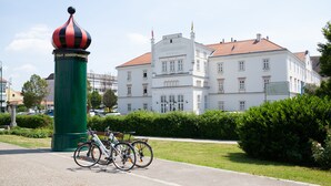Un edificio histórico con estilo arquitectónico clásico, una columna verde destacada con un adorno en la parte superior, y bicicletas estacionadas al frente.