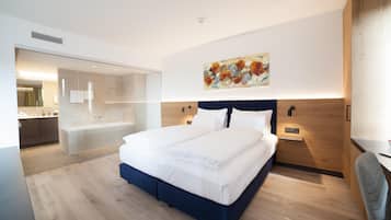Una camera d'albergo moderna con un letto grande, una cabina doccia in vetro e una testiera in legno.