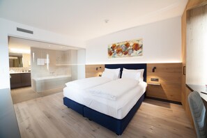 Une chambre d’hôtel moderne avec un grand lit, une douche en verre et une tête de lit en bois.