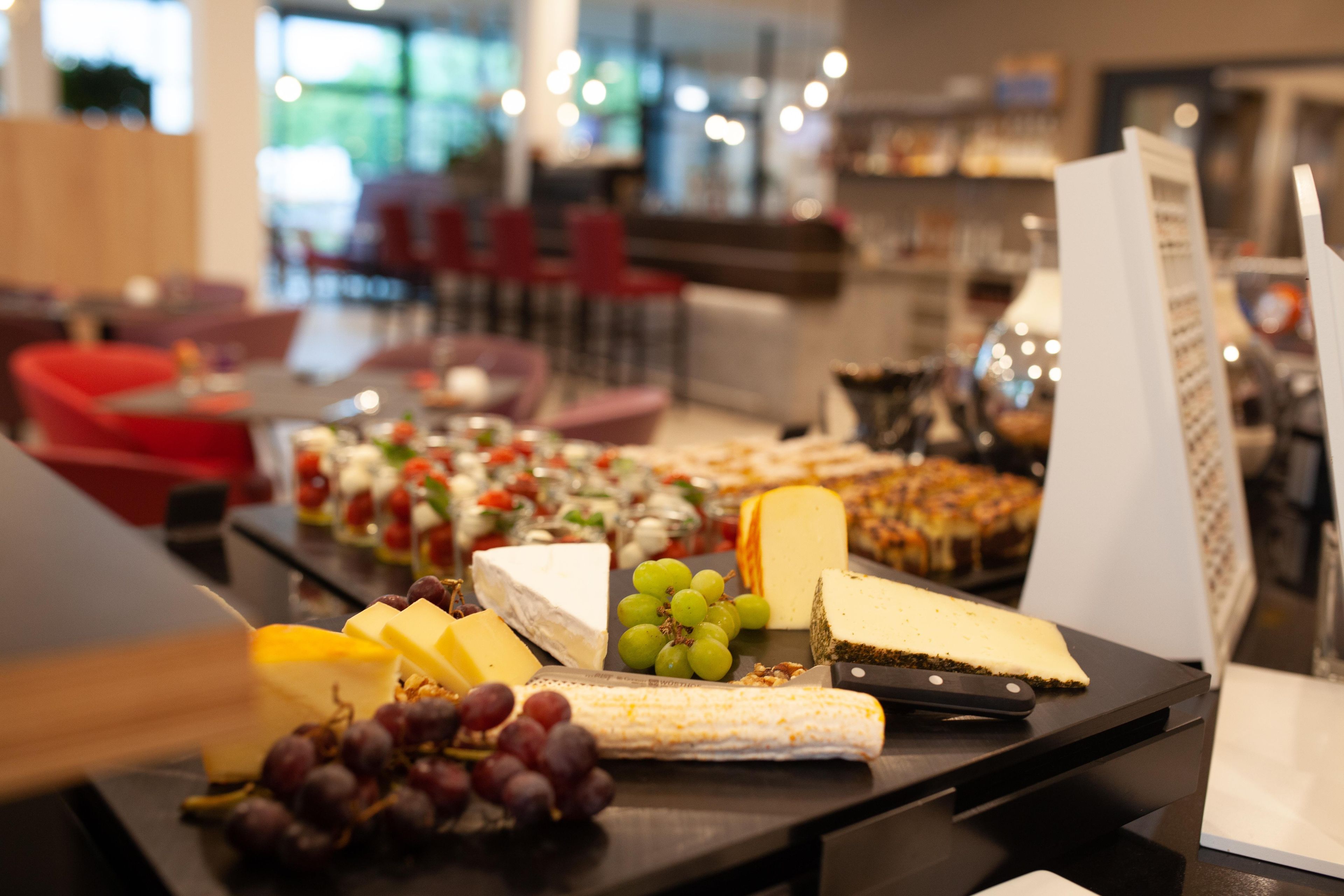 A buffet table with various cheeses, fruits, and a knife.