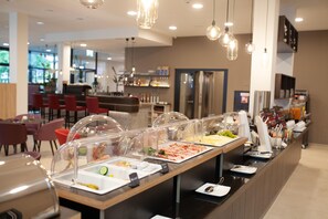Ett område med en buffé med olika matalternativ, en sittgrupp med röda stolar och en bar i bakgrunden.
