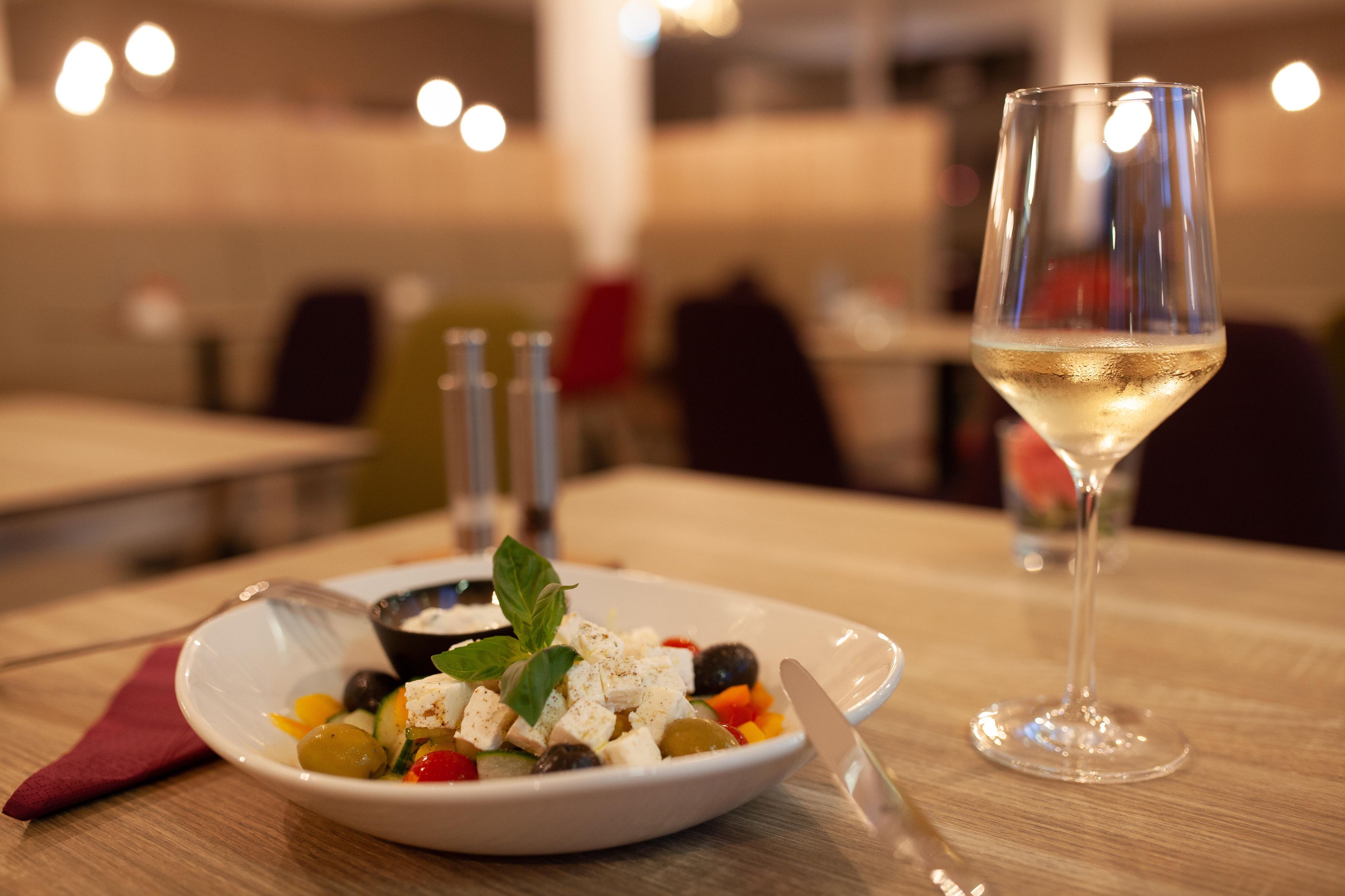 A dining table with a plate of food and a glass of white wine.