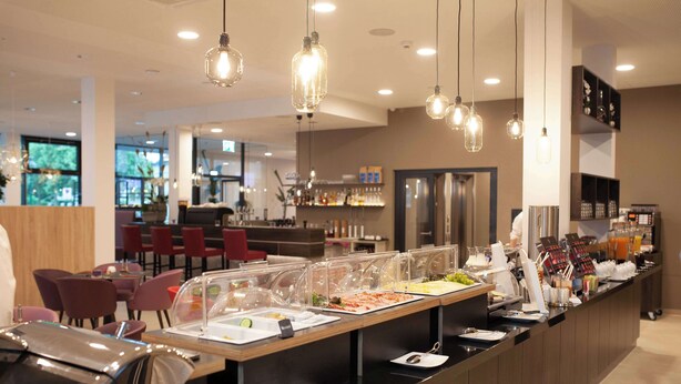 Un área de bufé con diversas opciones de comida, una zona de estar con sillas y un bar al fondo.