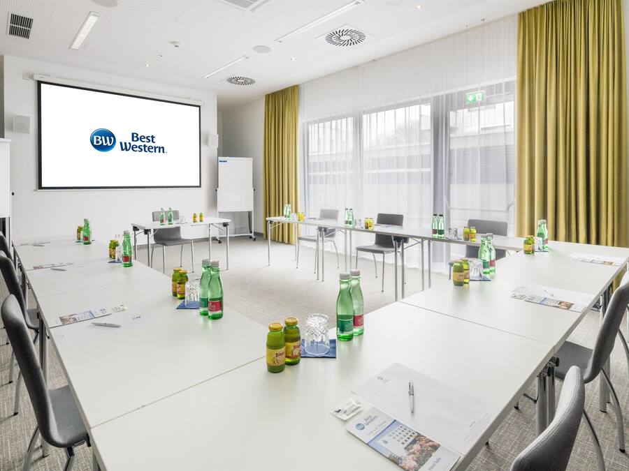 A conference room with a large screen displaying 'Best Western' logo, multiple tables with chairs, and various beverage bottles.