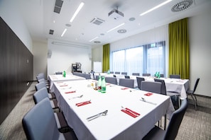 Ein Konferenzraum mit mehreren Tischen, Stühlen und einer Projektionsleinwand.