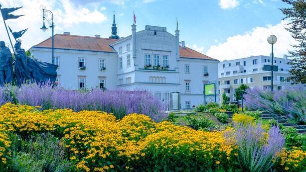 Un edificio histórico con techo de tejas rojas, paredes blancas y un balcón con jardineras florales.
