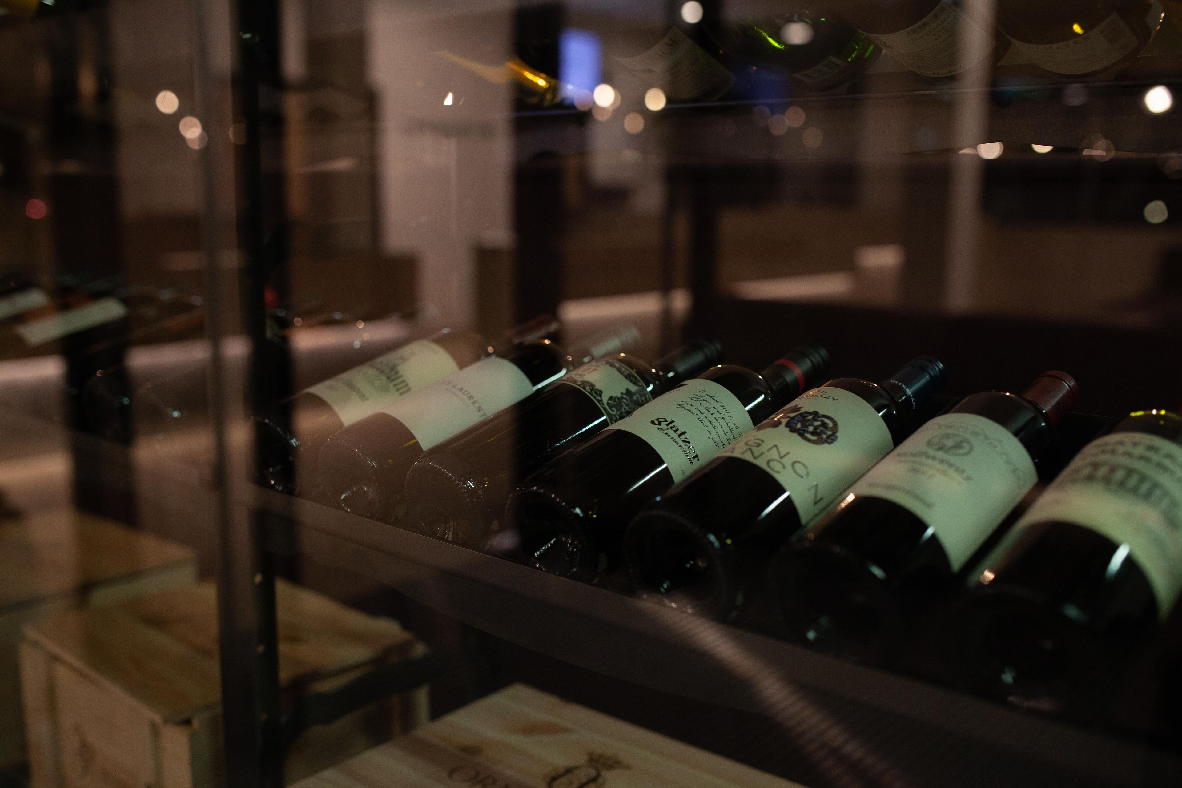 A row of wine bottles in a dimly lit room with a reflective surface in the foreground.