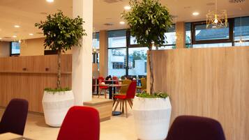 Et moderne spiseområde med træ skillevægge, røde og grønne stole samt store hvide plantekasser med grønne planter.