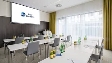 A conference room with a large screen displaying the Best Western logo, multiple tables with chairs, and various beverages on the tables.