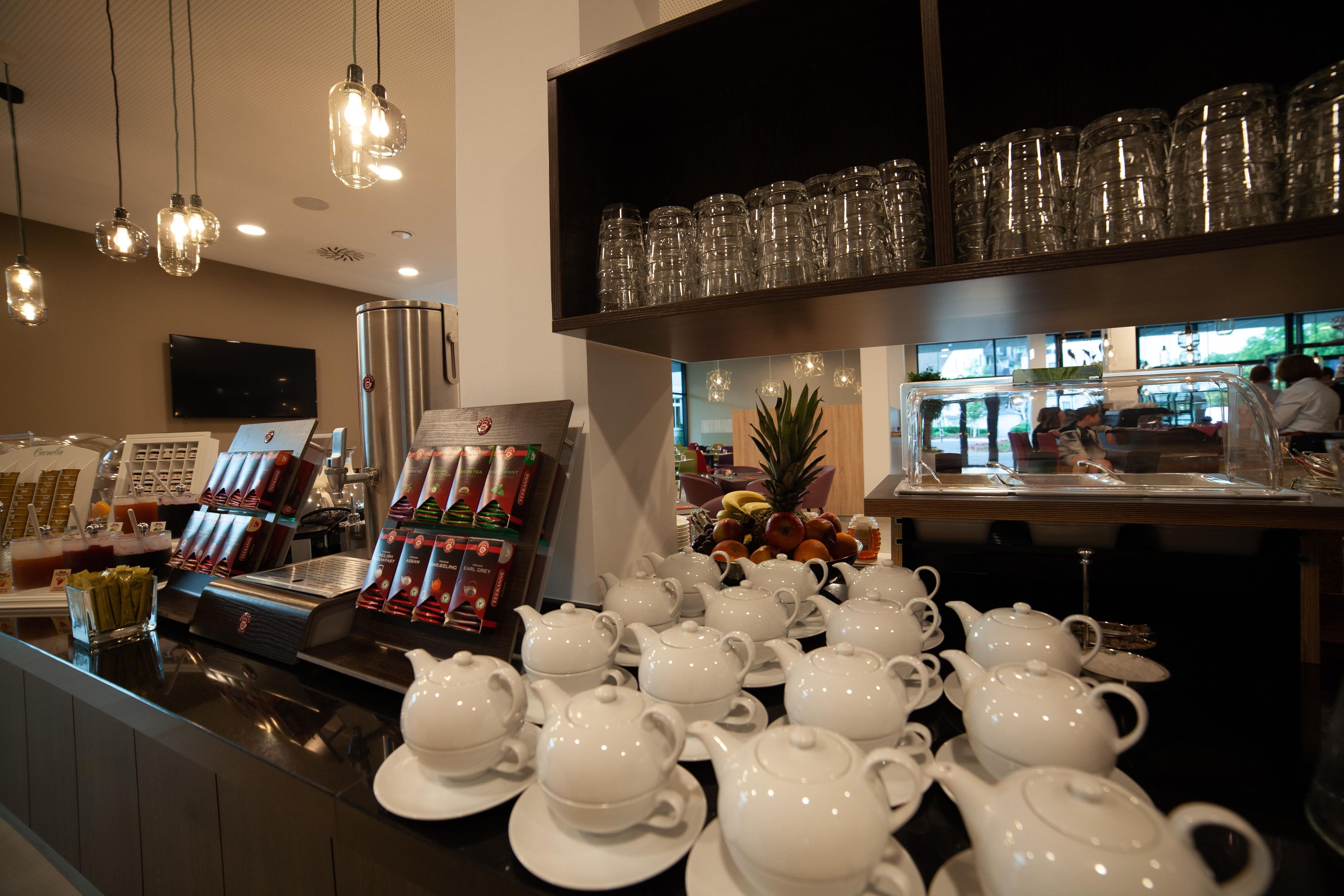 A tea station with multiple teapots and cups, a selection of bottled beverages, and a fruit display.