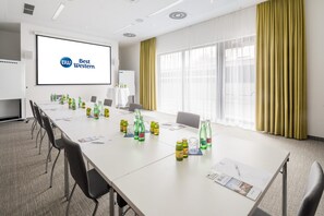 Ein Konferenzraum mit einem langen Tisch, Stühlen, einer Projektionsleinwand und einer Whiteboard-Tafel.