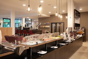 Un espace buffet proposant une variété de plats, avec différentes options de places assises et un bar en arrière-plan.