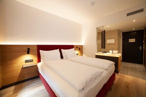Ein Hotelzimmer mit einem großen Bett, einem Holzkopfende, einem Nachttisch mit Lampe, einem Spiegel und einem Badezimmer mit Waschbecken und großem Spiegel.