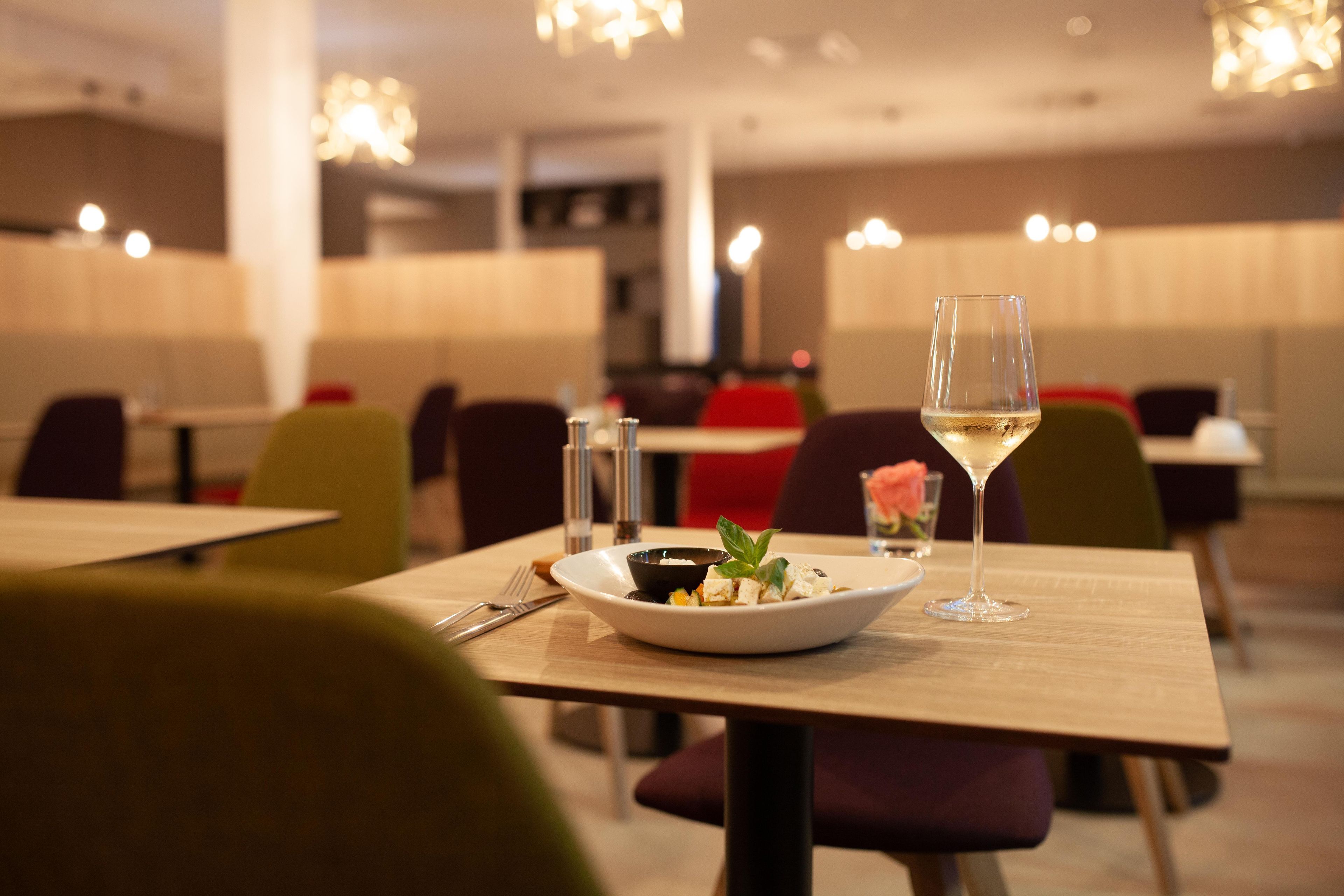 A dining table with a plate of food, a glass of white wine, and cutlery.