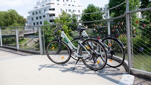 Una bicicleta estacionada en un puente con una cerca de alambre adornada con candados de colores.