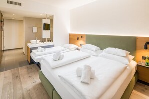 Ett hotellrum med två sängar, ett badrum med handfat och spegel samt en sänggavel i trä.