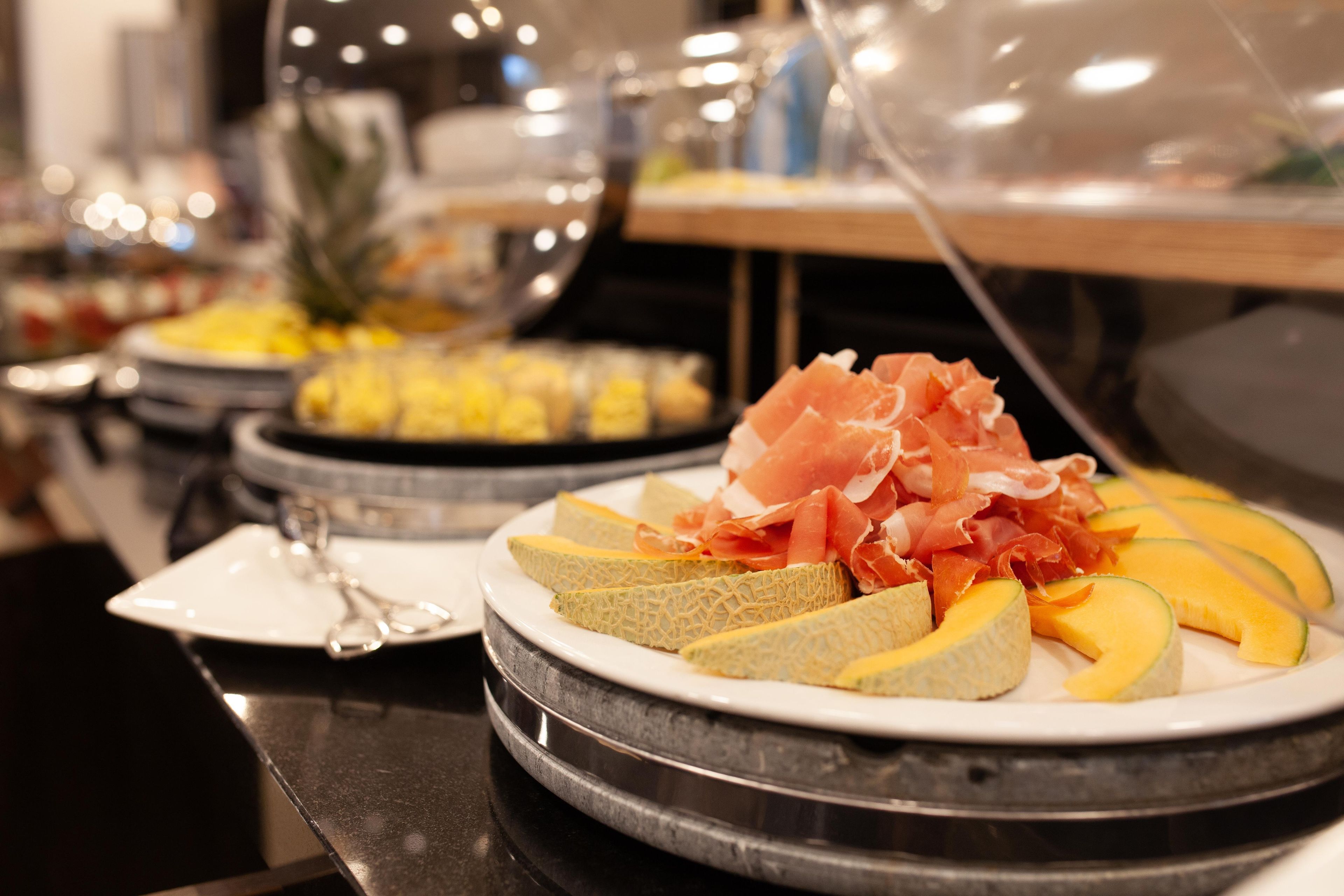 A buffet with various food items including melon slices and prosciutto.