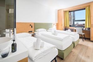Ein Hotelzimmer mit zwei Betten, einem Schreibtisch, einem Stuhl, einem fenster mit Vorhängen und Blick auf ein Gebäude.