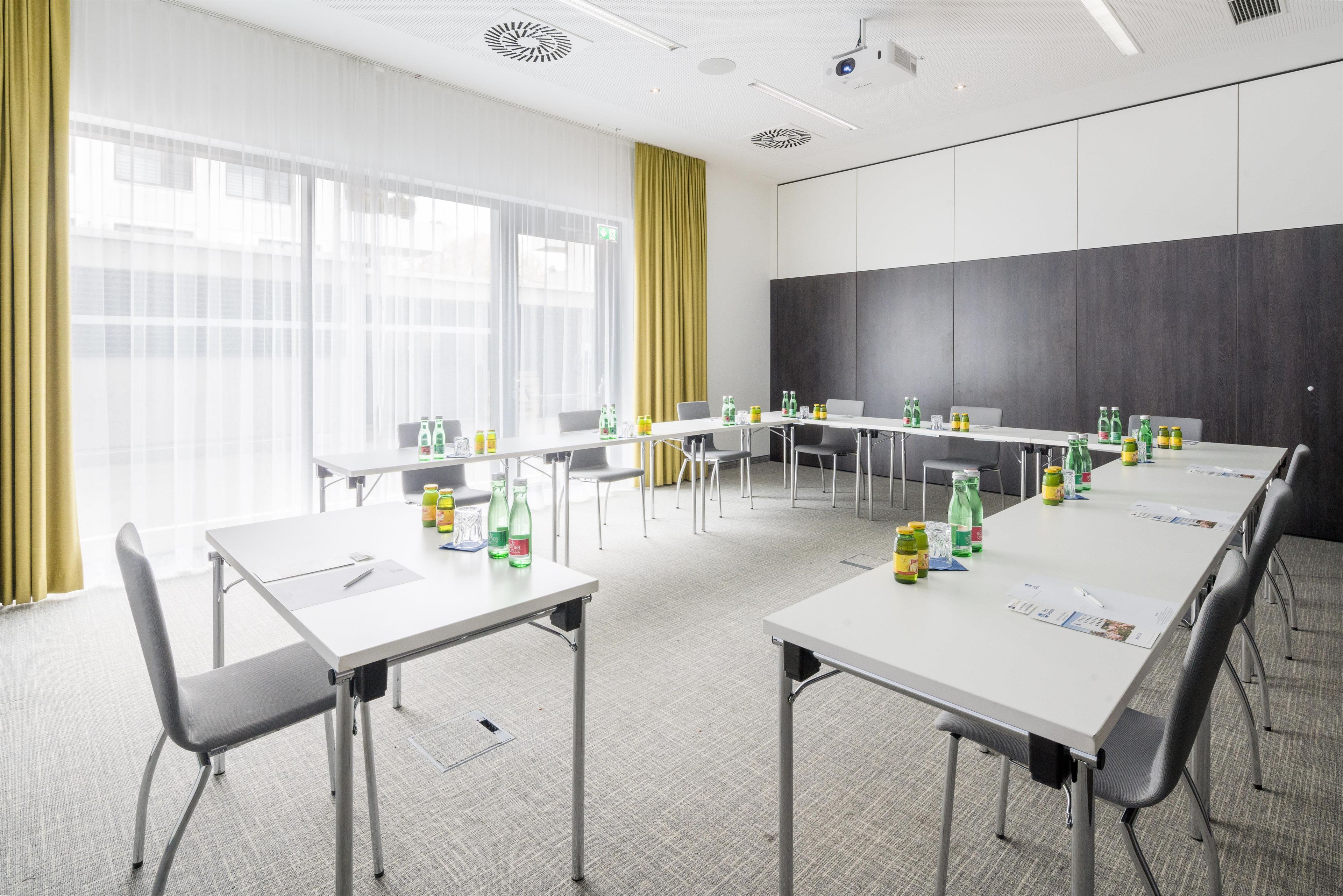 Ein Konferenzraum mit weißen Tischen, Stühlen und einer Projektionsleinwand.