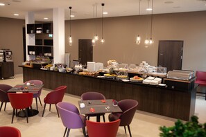 Eine moderne Frühstückstheke mit vielfältigen Speisen, umgeben von Sitzgelegenheiten mit roten und violetten Stühlen.