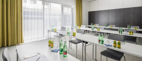 Un salón de conferencias con mesas y sillas blancas, y una pantalla de proyector.