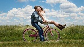 Una pareja en bicicleta en un campo cubierto de hierba, con cielo despejado.