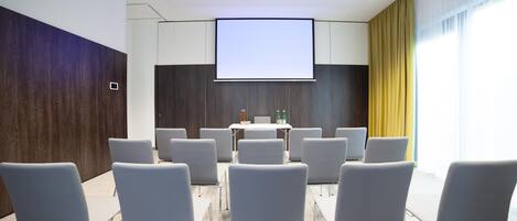 Une salle de conférence équipée d’un grand écran, de nombreuses chaises et d’une table sur laquelle sont posées des bouteilles.