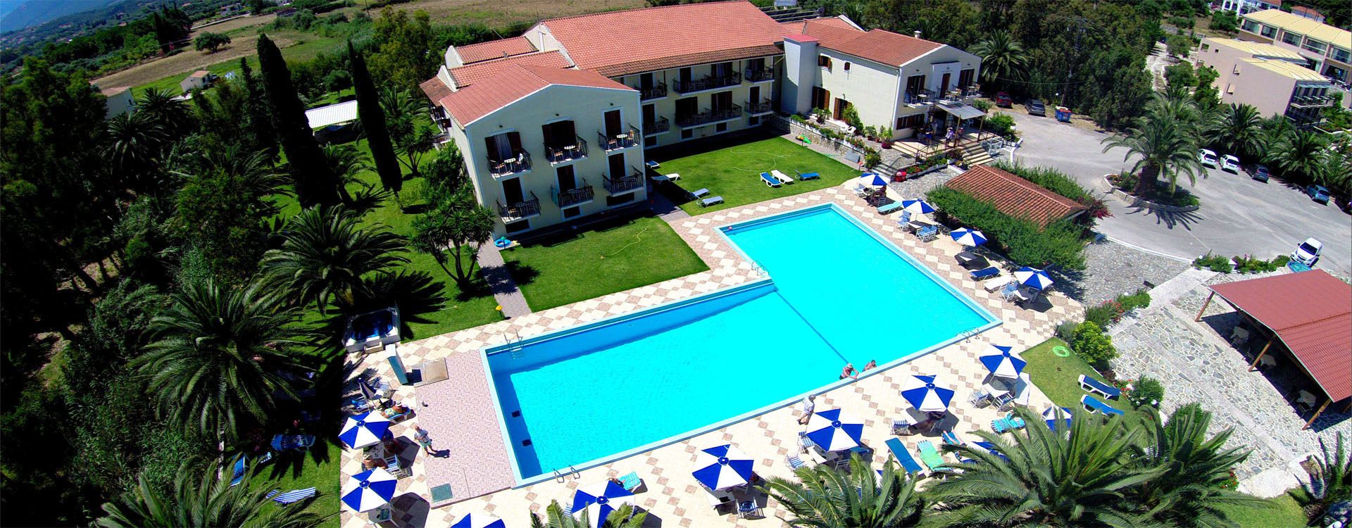 A large swimming pool with sun loungers and umbrellas, surrounded by a well-maintained lawn and palm trees.