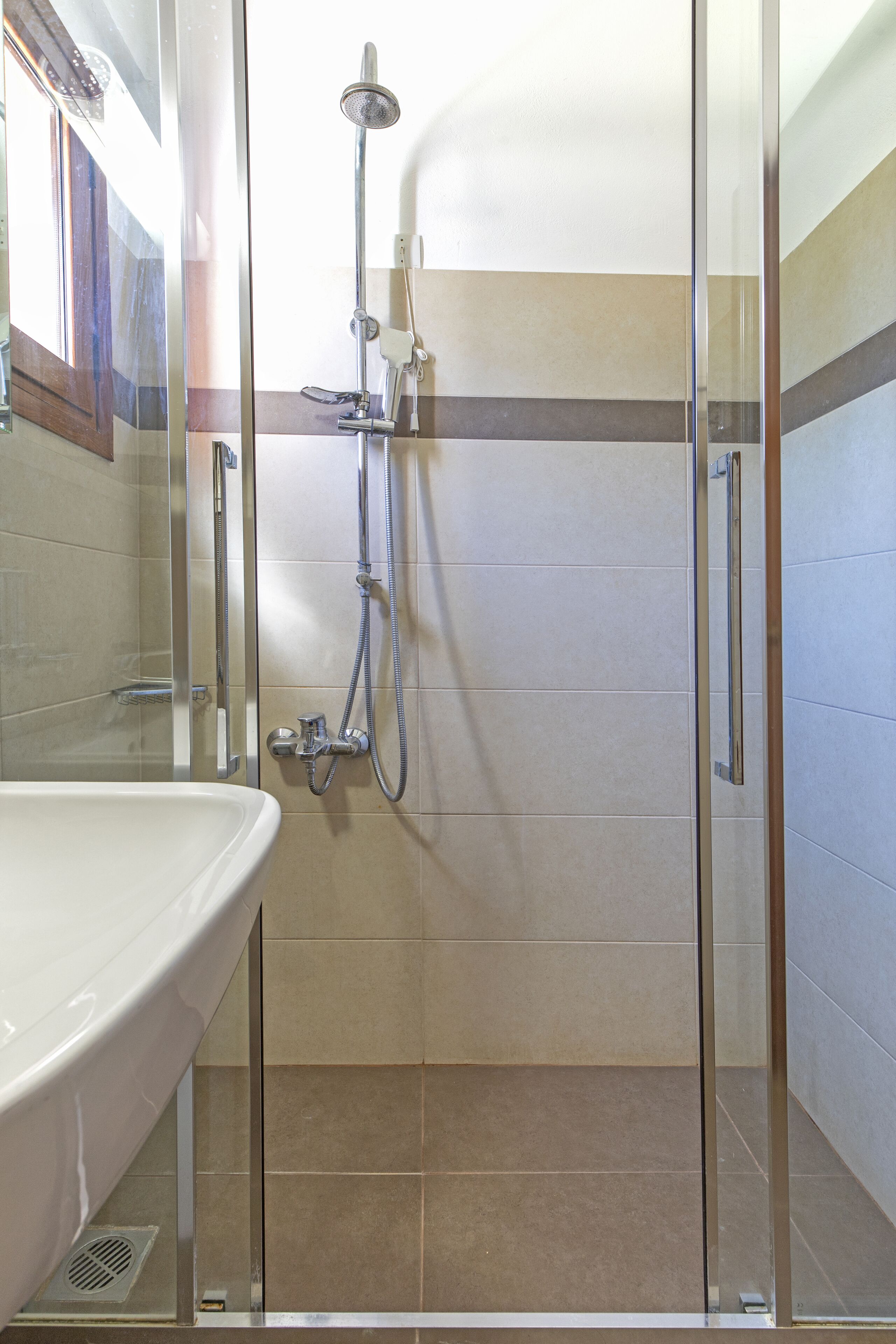 A bathroom with a glass-enclosed shower, a white sink, and tiled walls.
