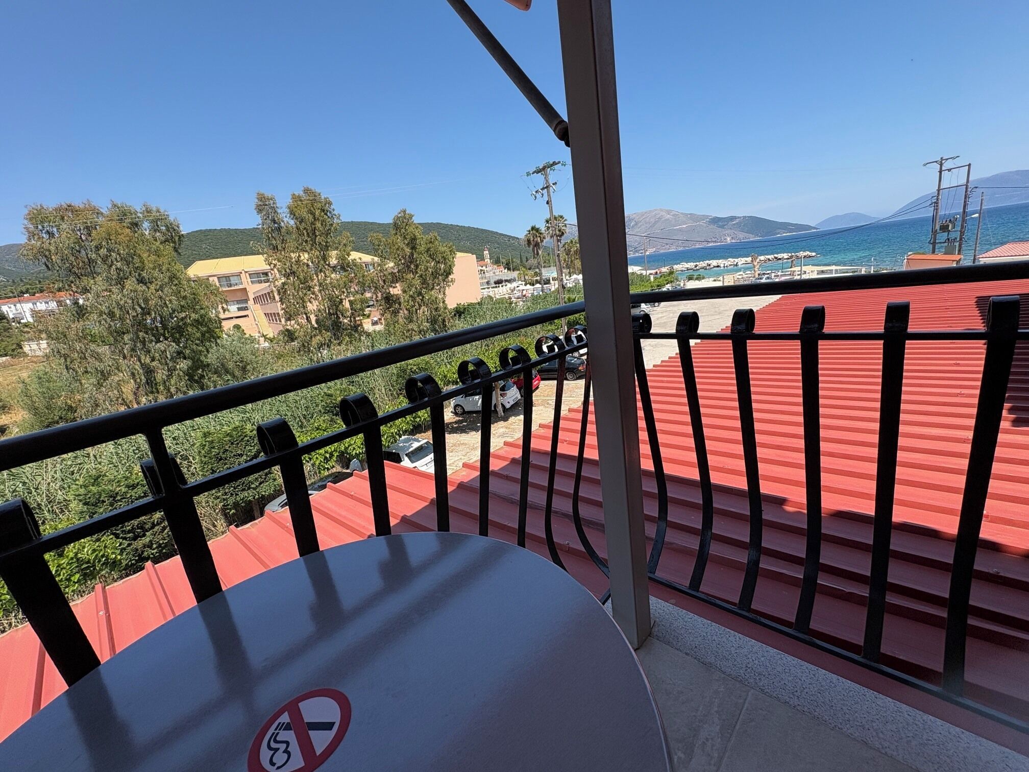 Un balcón con techo rojo, un letrero de no fumar y vistas a la playa y las montañas.
