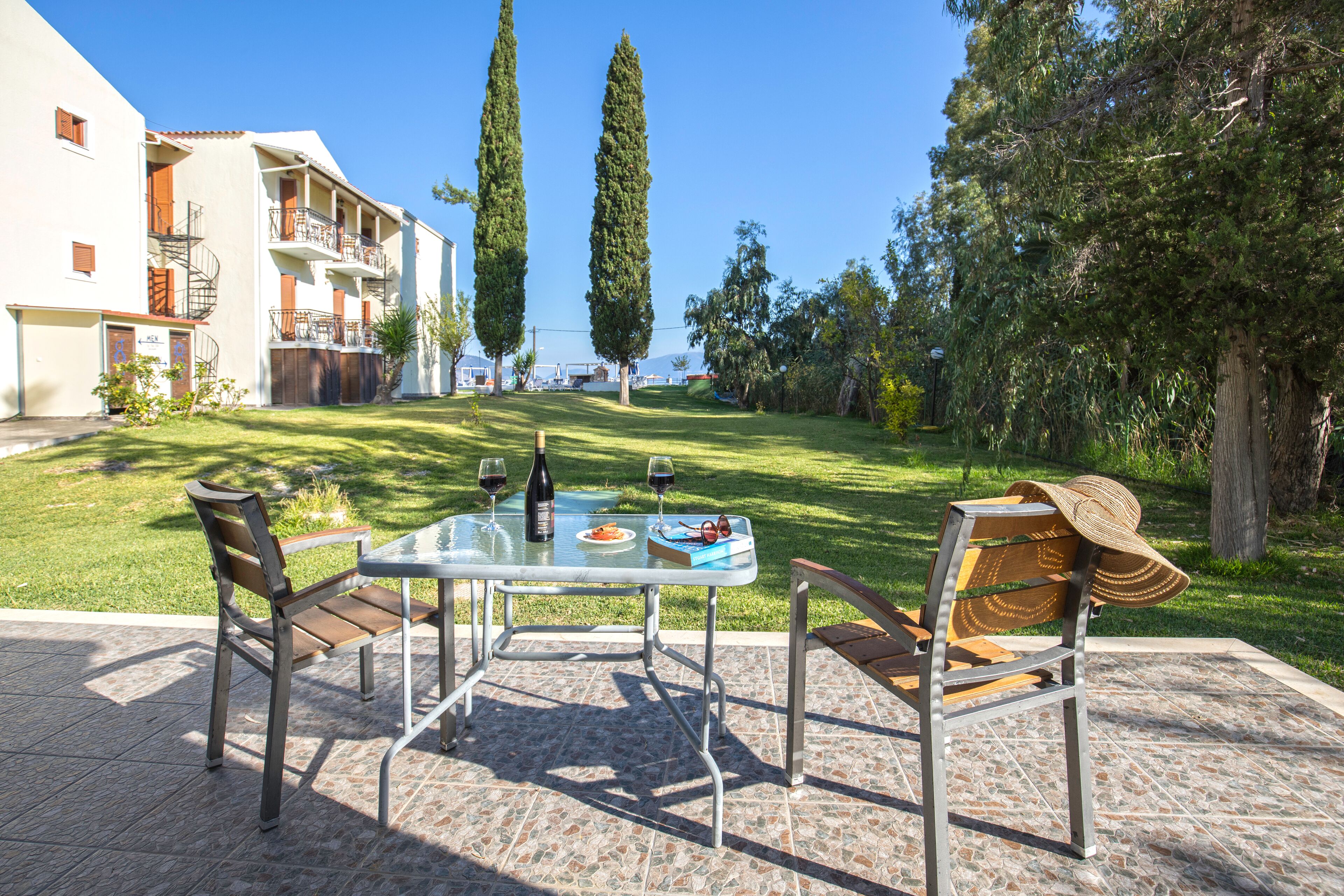 An outdoor patio with a table set for two, two chairs, and a hat on one of the chairs.