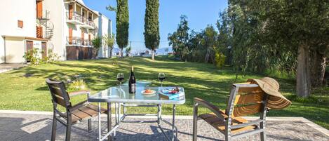 An outdoor patio with a table set for two, two chairs, and a hat on one of the chairs.