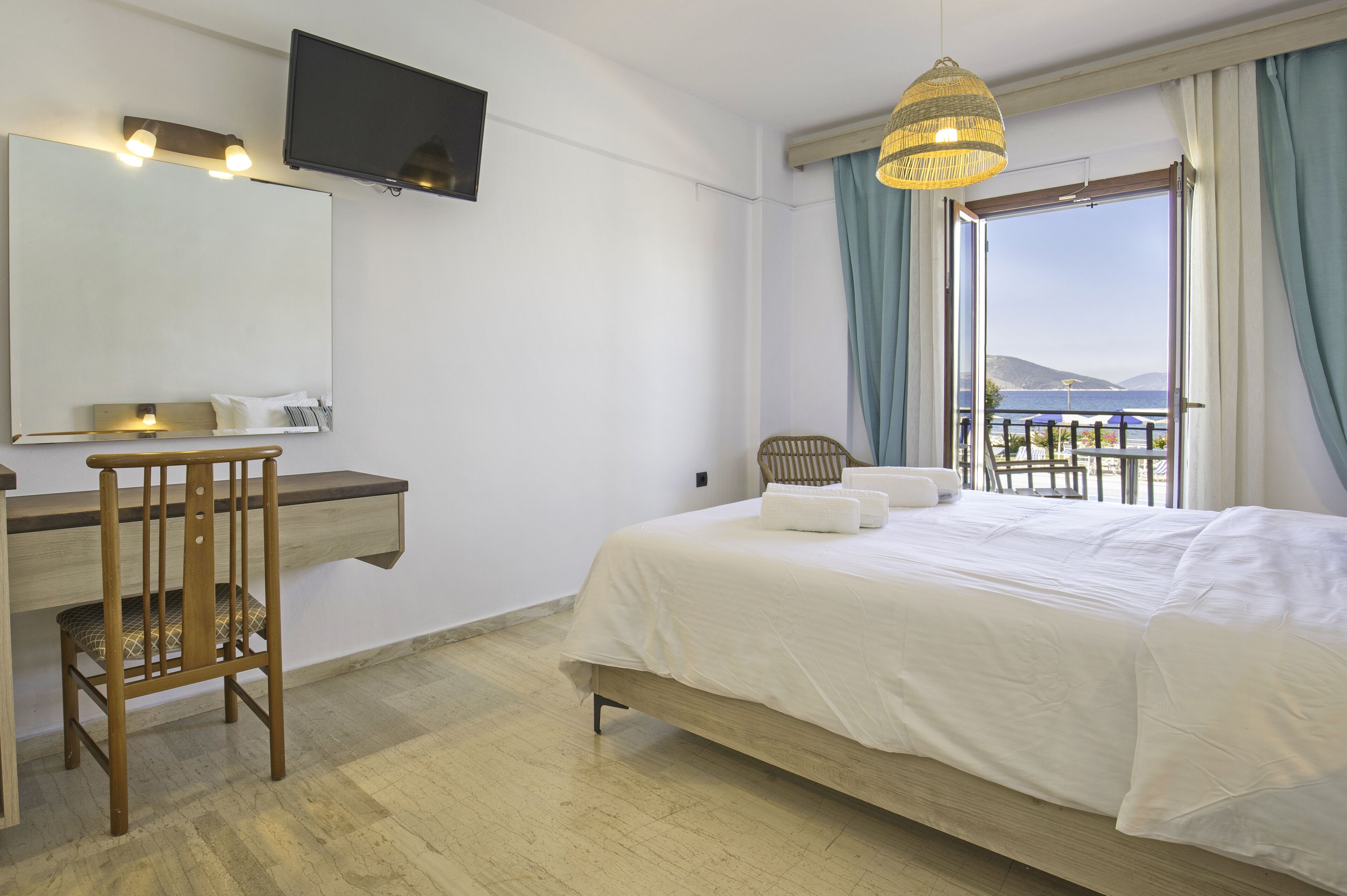 A hotel room with a bed, a desk, a chair, a television, and a view of the sea.