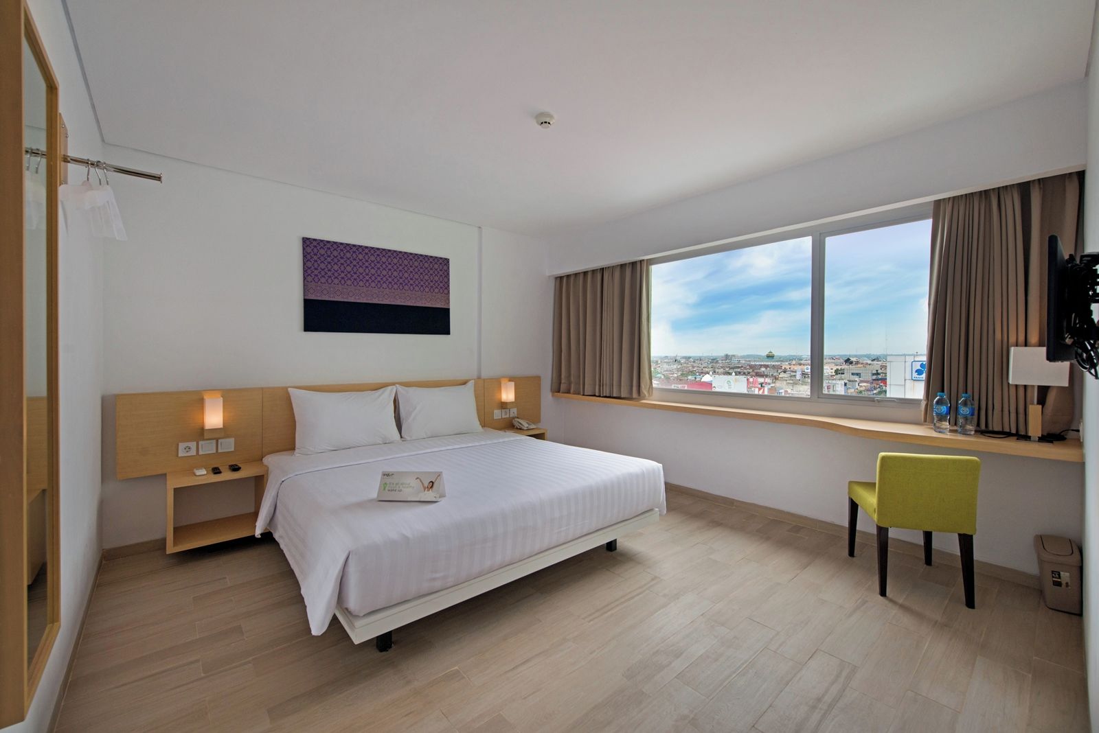 Habitación de hotel con cama, mesitas de noche, escritorio con silla, ventana con vistas y televisor de pared.