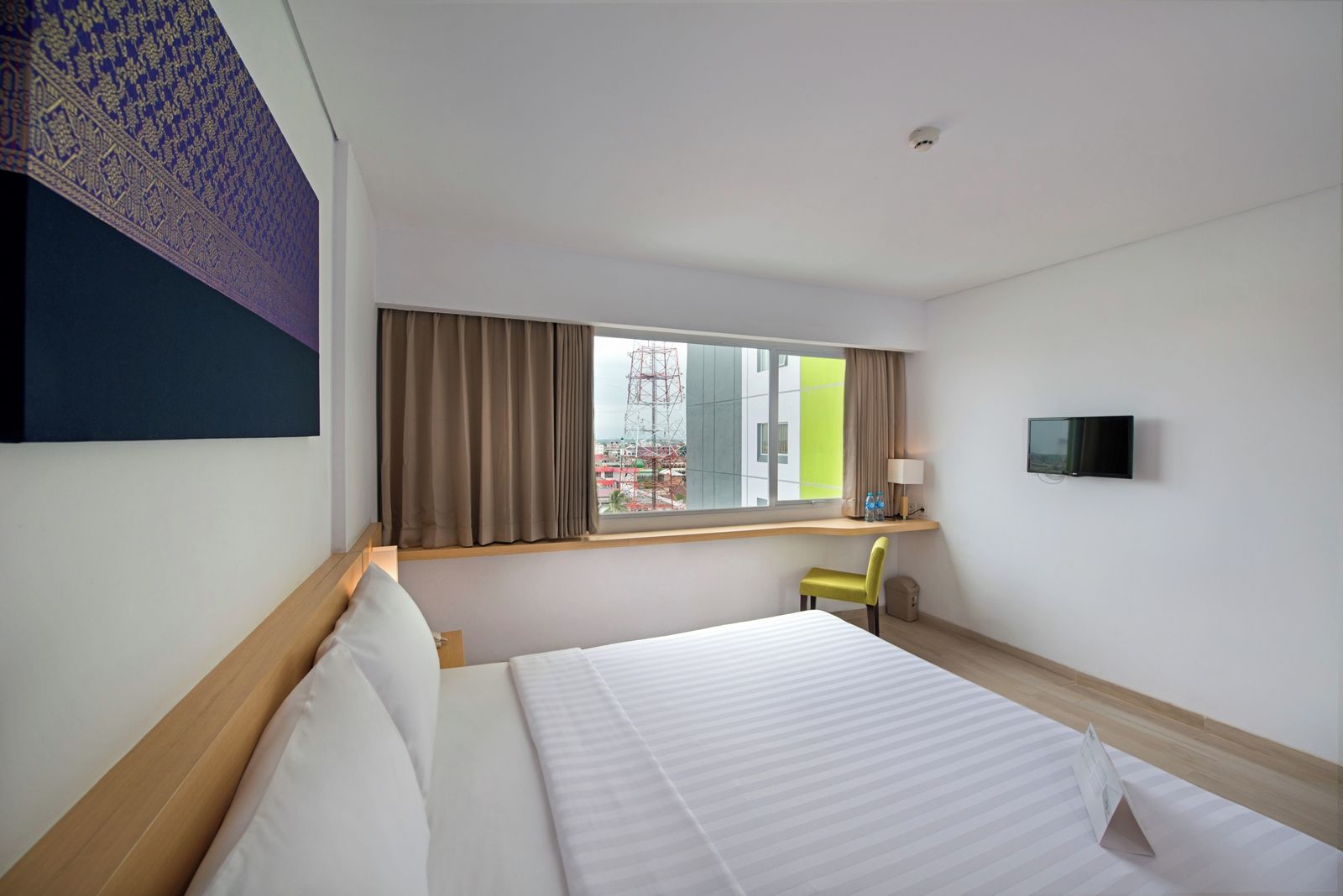 A hotel room with a bed, a desk with a chair, a TV, and a window with curtains.