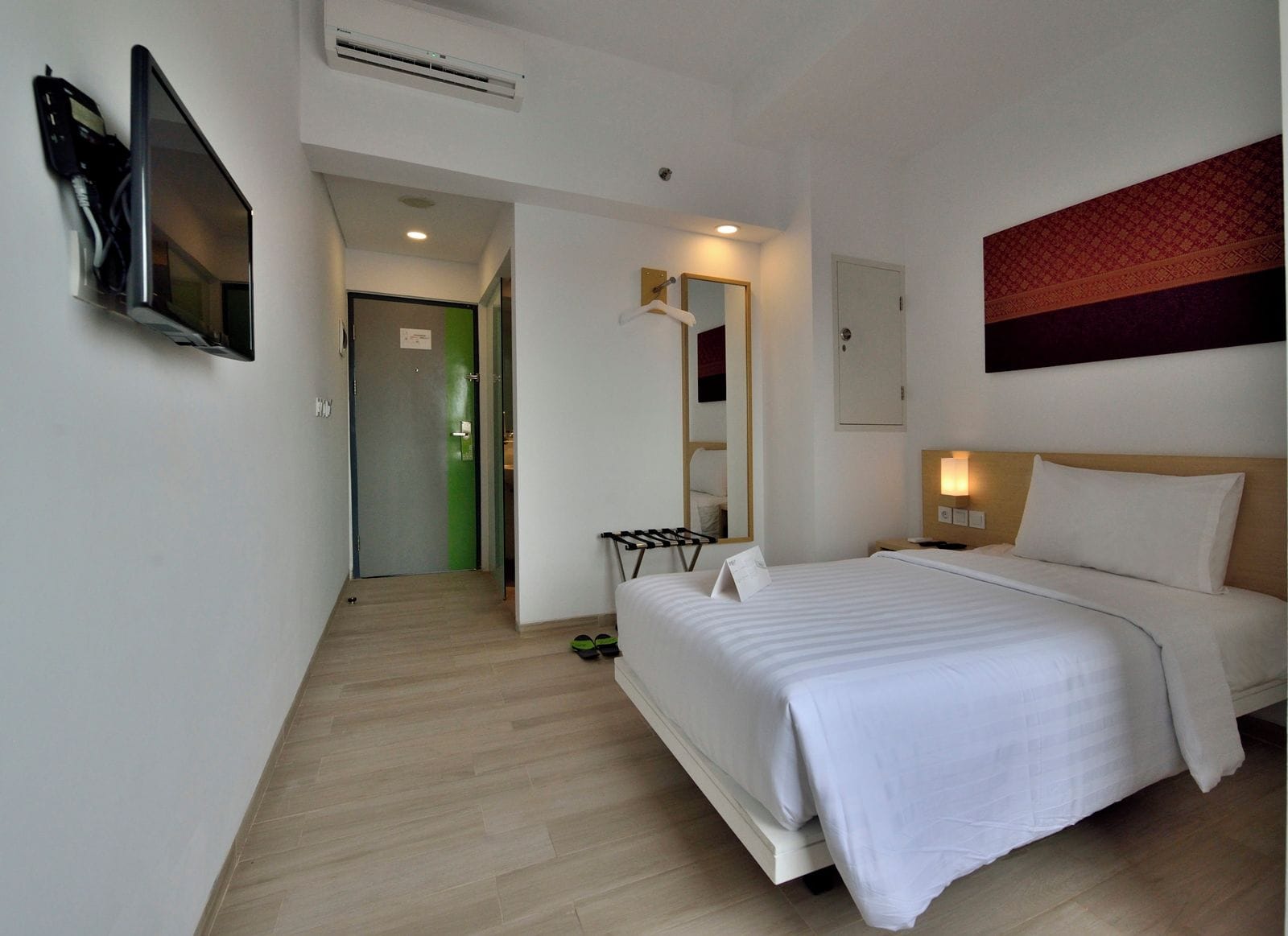 A hotel room with a bed, a TV mounted on the wall, a mirror, and a door leading to another room.
